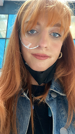 A woman featuring bright red hair in hospital, gazing directly at the viewer with a bold look.