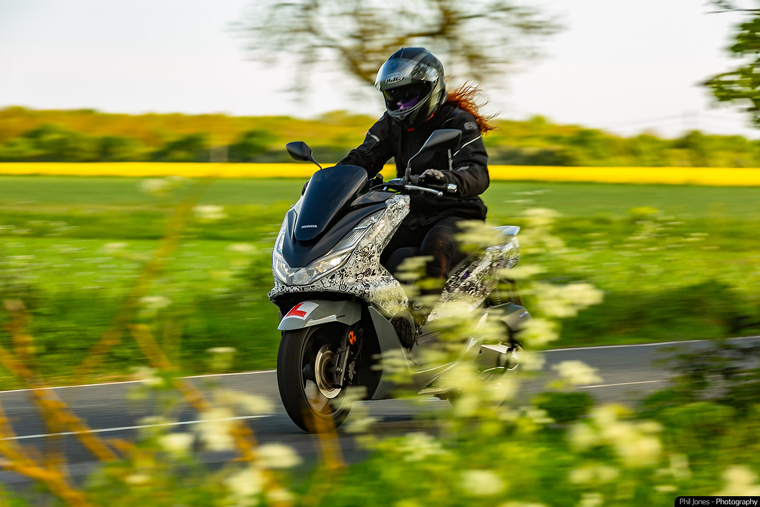 A woman rides a motorcycle through the country lanes