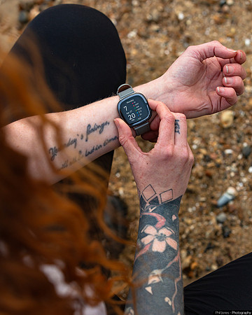 A woman with arm tattoos checks her Fitbit watch, worn on the inside of her wrist.