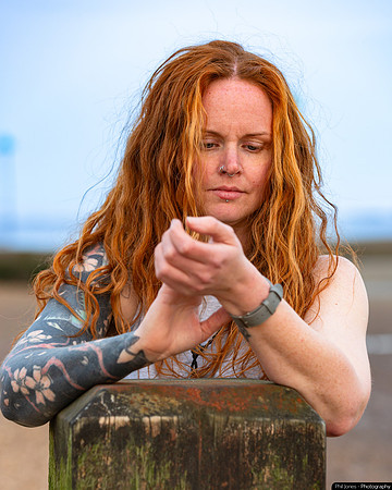 A redheaded woman standing on a beach checks her smartwatch worn on the inside of her wrist
