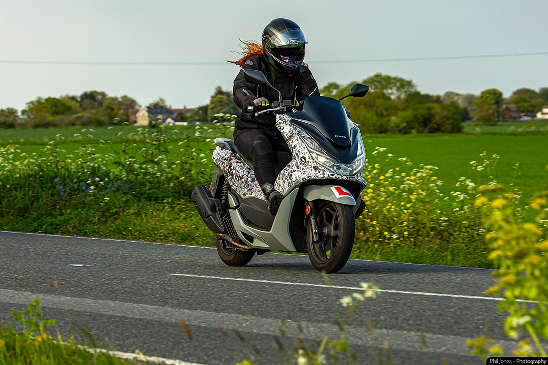 A person riding a motorcycle along a winding road surrounded by trees and open fields.