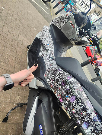 A woman gives a thumbs up to her scooter covered in stickers