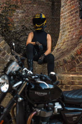 A female motorcyclist sits on a viaduct arch wearing her motorcycle clothing and crash helmet