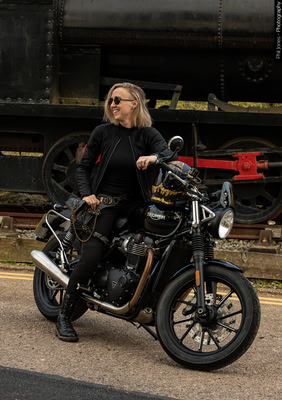 a woman sits on her motorcycle laughing, there's a train in the background