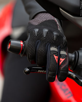 a womans hand wearing Dainese motorcycle gloves, she holds the grip with fingers on the front brake