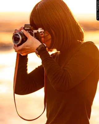 a woman takes a photo with an analog camera as she stands against a setting sun