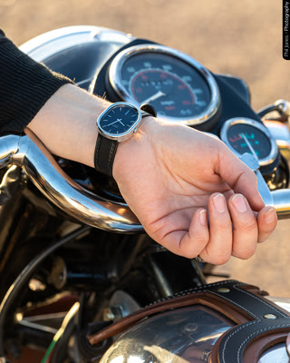a woman leans her hand on her motorcycle handlebars showing her wrist watch worn inside the wrist
