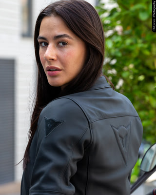 a woman wears a black motorcycle jacket showing speed demon logo on back and arms