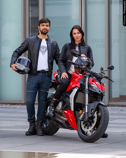 A man and a woman stand proudly beside a motorcycle.
